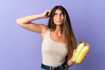 Obraz premium Young woman holding corn isolated on purple background having doubts and with confuse face expression