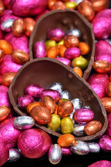 Pile of  colourful foil wrapped chocolate easter eggs in pink, red, gold, silver and orange with two halves of a large brown milk chocolate egg in the middle and mini eggs inside.