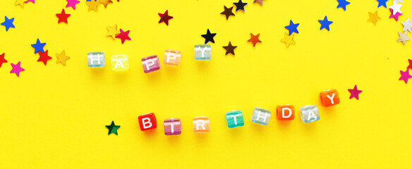 inscription happy birthday and multicolored confetti in the form of stars on yellow background