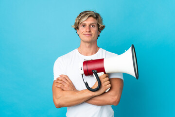 English man over isolated blue background holding a megaphone and smiling
