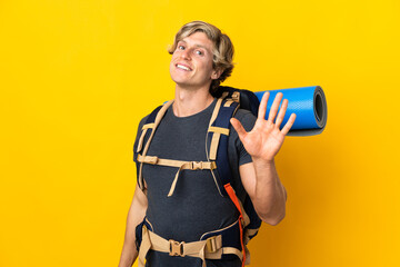 Young mountaineer man over isolated yellow background saluting with hand with happy expression