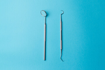 The concept of oral health. Diagnostic bilateral periodontal probe and diagnostic dental mirror made of stainless steel. Dental equipment highlighted on a turquoise background, close-up. Top view