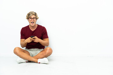Obraz premium Young English man sitting on the floor surprised and sending a message
