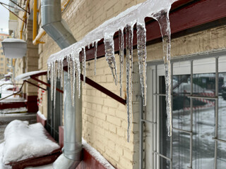 long icicle that hangs on the roof edge and melts. Drops of water run down the melting icicle. Springtime theme.