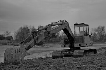 A tracked excavator during a break in works on a water reservoir. - obrazy, fototapety, plakaty