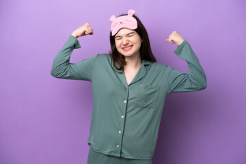 Young Russian woman in pajamas isolated on purple background doing strong gesture