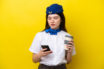 Airplane stewardess Russian woman isolated on yellow background holding coffee to take away and a mobile