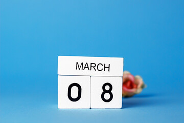 Calendar with white wooden date made from cubes. March 8. International Women's Day. Blue background and a bouquet of pink roses.