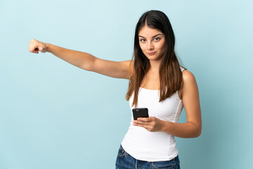 Young caucasian woman using mobile phone isolated on blue background giving a thumbs up gesture