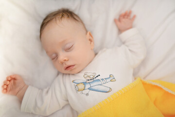 Top view sleeping newborn baby lies in a crib arms outstretched, baby sleep. Baby sleeping in bed. Infant baby sleeping on white sheets. 