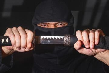 Ninja ready to fight, holding a Japanese sword. Photo of a warrior dressed in black clothes and...