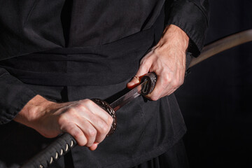 The samurai holding a Japanese katana sword. Photo of a warrior dressed in black clothes in low key...