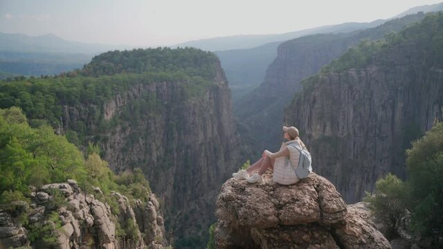 The girl admires the beautiful view in the mountains . the girl is sitting on the edge of a cliff on a rock looking into the distance. Tazy Canyon in Turkey. The tourist destination is Turkey.