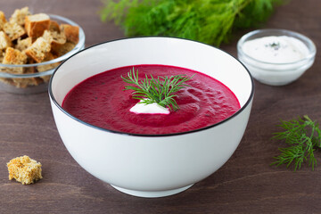 vegetable soup with greens and croutons. white bowl of Beetroot cream soup with bread and white cream on a wooden background. Healthy diet lunch with copy space.