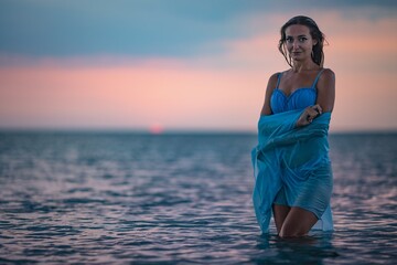 A girl in a blue swimsuit and a bright pareo posing against the background of a sunset in estuary with transparent water