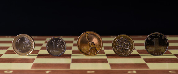 Coins of denominations of 1 euro, 1 ruble, 1 pound, 1 dollar and 1 yuan on a chessboard