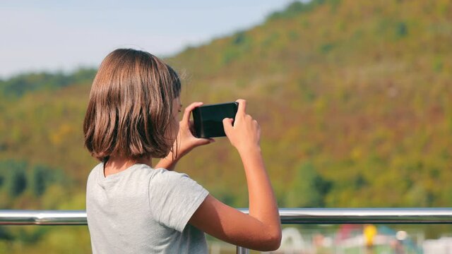 Teen girl takes pictures with a mobile phone while traveling on a ship. The girl takes pictures on her mobile.