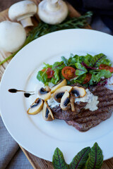 Pieces of fried meat lie on a white plate and drizzled with white sauce. Decorated with vegetables, mushrooms and herbs. The concept of recipes from the restaurantf.