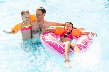 Happy family playing in blue water of swimming pool on a tropical resort at the sea. Summer vacations concept.