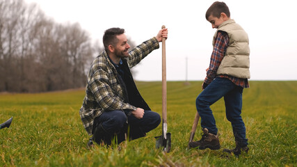 Naklejka na ściany i meble The dad with his little son planting a tree in the field