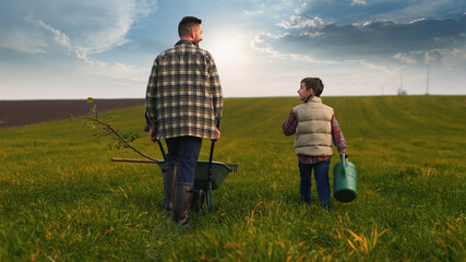 The farmer with his little son walking through the green field