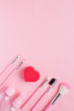 A cute arrangement of makeup items in pink with a heart-shaped sponge. Advertising concept for makeup artist for valentine's day. Vertical photo, flat lay, top view