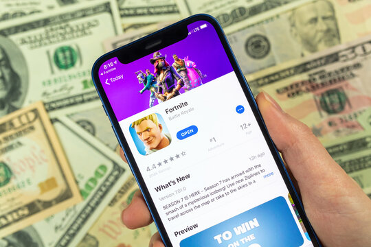 Person uses Apple iPhone for playing Fortnite game. Icon close-up, money, dollar bills business background photo