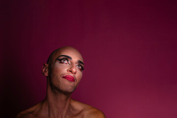 Beautiful transgender gay man wearing makeup looking up, isolated on pink background; with copyspace