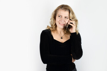 Pretty woman with blond hair in a dark blouse talks on the phone and smiles, she is happy to hear...