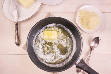 Cooking homemade Alfredo pasta. Melted butter in a frying pan and grated parmesan cheese, top view