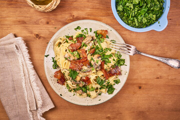 Pasta with mushrooms and fried pancetta. Classic Italian fettuccine with creamy mushroom sauce, fried bacon and fresh parsley on a platter, top view