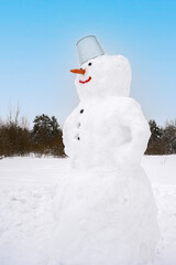 Cute smiling snowman in the field covered with snow.