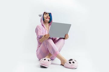 A woman in a unicorn pajamas sitting on the floor and holding a laptop