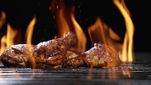 Chicken drumsticks or legs grilled on hot barbecue charcoal flaming grill with spices sprinkled on top. Juicy chicken meat roasted on bbq grill. slow motion