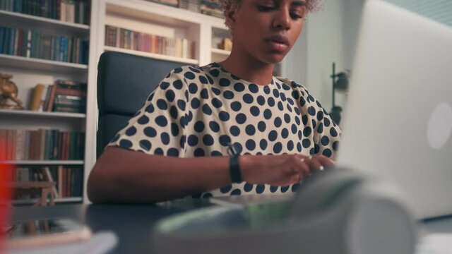 Young successful African American business woman typing on laptop then leaning back in chair thinking about own company sits at desk in office. Entrepreneurship, professionalism, freelancing concept