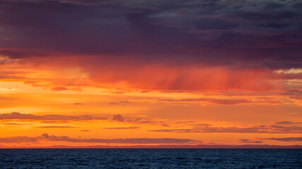 Dramatic orange cloudscape over deep blue water at sunset