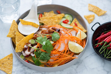 Grey plate with nachos chips, barbecue chicken meat, vegetables and dip sauce over light-grey marble background, horizontal shot