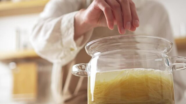 Glass transparent pot with boiling water, spaghetti. Female chef adds salt pasta. Cooking at home, food or culinary blog. Woman mixes spaghetti pasta in saucepan with salt. Italian dinner preparation
