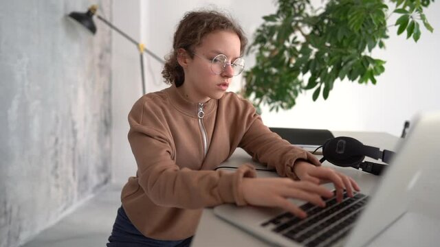 Side view of serious teen girl working with laptop in coworking space. Doing homework, chatting with friends on social networks, surfing the Internet