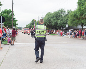 Police officer on duty walking along street at public July 4 parade event near Dallas, Texas, America