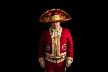 Mexican mariachi musician covering half of his face with a sombrero on a black background