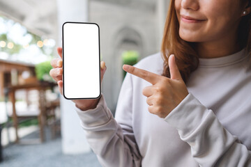 Fototapeta Mockup image of a young woman holding and pointing finger at a mobile phone with blank white screen obraz