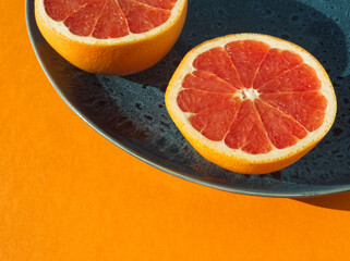 Half pink sliced grapefruit on blue plate on orange background. Citrus pink fruit. Modern food...