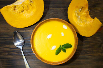 Homemade pumpkin soup in a clay bowl with cream and seeds lay on a brown wooden rustic background