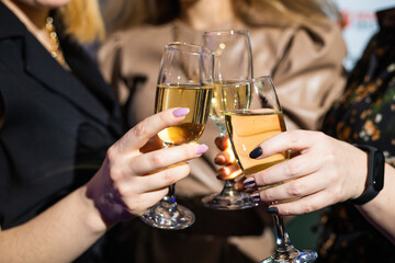 close up glasses of clinking glasses of champagne with lighting. Dinner party with drinking of champagne. hands holding clear glass with alcohol in yellow shine reflect.