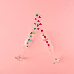 Creative composition made of champagne glasses with shiny heart shaped glitter against pink background. Minimal Valentine's day celebration concept. Love aesthetic. Top view. Copy space.