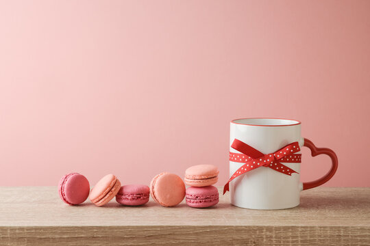 Valentines day concept with coffee cup, heart shape and macaroons dessert on wooden table over pink background