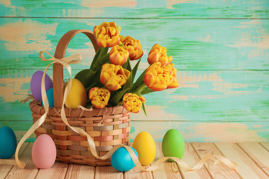 Easter composition with Easter eggs and tulip flowers in basket on wooden table. Greeting card for holiday celebration