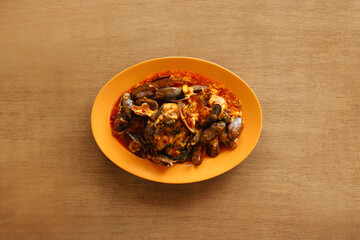 Spicy seafood sambal mussels with raw onion and chili pepper in orange plate on wood table background top view food