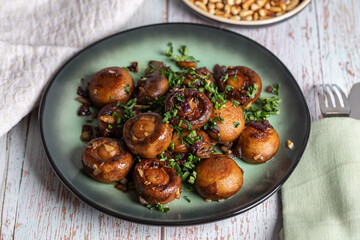 Plate of fried mushrooms with dill, garlic, pine nuts and parsley on the wooden table